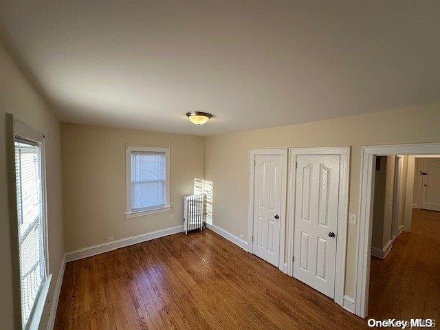 unfurnished bedroom with radiator, dark hardwood / wood-style flooring, two closets, and multiple windows