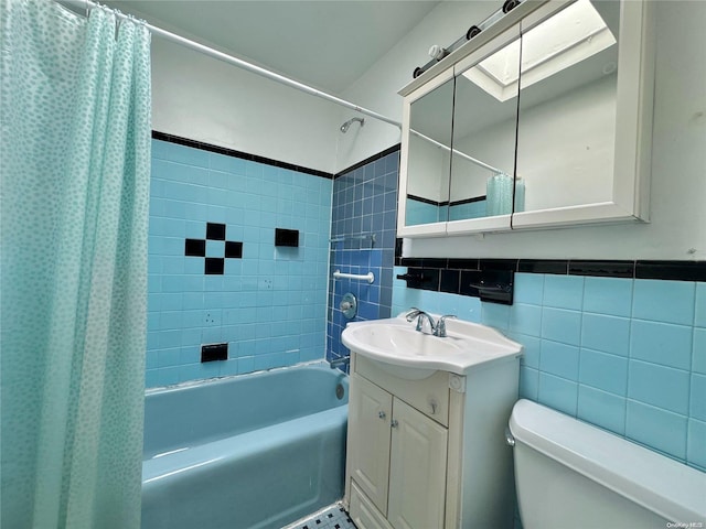 full bathroom with a skylight, vanity, tile walls, shower / bathtub combination with curtain, and toilet