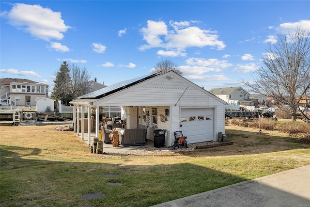 back of property with an outbuilding, a garage, a lawn, and solar panels