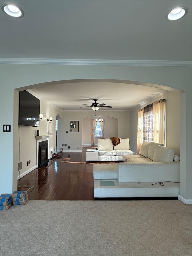 unfurnished living room with ceiling fan, ornamental molding, and dark carpet