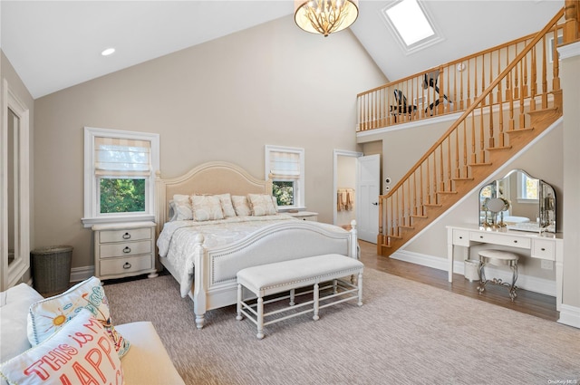 bedroom featuring hardwood / wood-style flooring, high vaulted ceiling, a skylight, and a notable chandelier