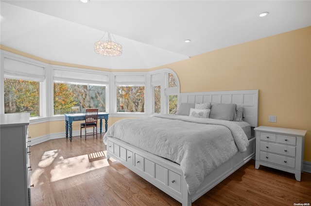 bedroom featuring wood-type flooring, lofted ceiling, and an inviting chandelier