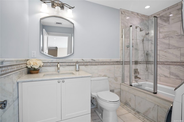 full bathroom with vanity, tile patterned floors, bath / shower combo with glass door, toilet, and tile walls