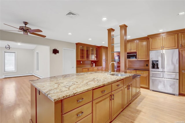 kitchen with light stone countertops, stainless steel appliances, a kitchen island with sink, sink, and light hardwood / wood-style floors