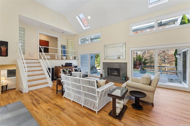 living room featuring light hardwood / wood-style floors, a tile fireplace, high vaulted ceiling, and a skylight