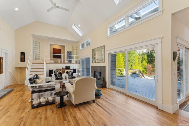 living room with a skylight, high vaulted ceiling, light hardwood / wood-style flooring, and ceiling fan