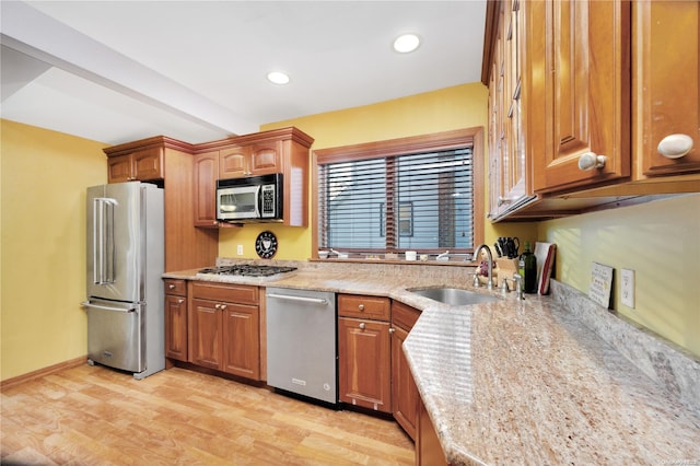 kitchen with light stone counters, sink, stainless steel appliances, and light hardwood / wood-style flooring