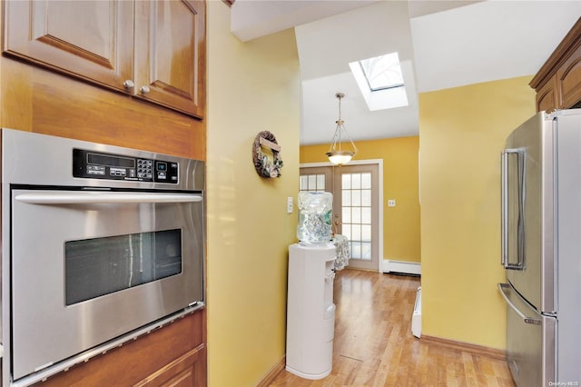 kitchen featuring pendant lighting, a skylight, light wood-type flooring, baseboard heating, and appliances with stainless steel finishes