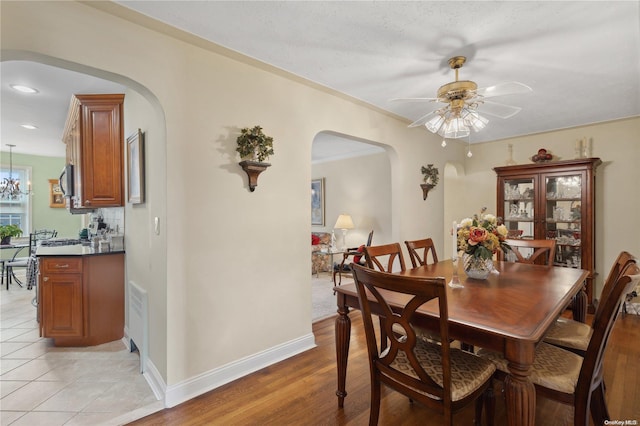 dining room with ceiling fan with notable chandelier, a textured ceiling, light wood-type flooring, and ornamental molding