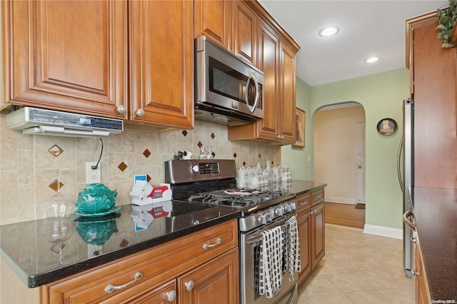 kitchen featuring dark stone countertops, light tile patterned floors, appliances with stainless steel finishes, and tasteful backsplash