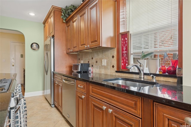 kitchen featuring light tile patterned flooring, appliances with stainless steel finishes, dark stone countertops, and sink