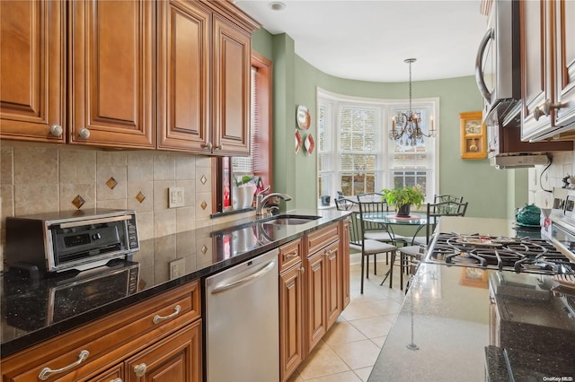 kitchen with sink, stainless steel appliances, dark stone counters, a chandelier, and light tile patterned floors