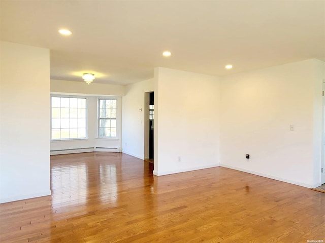 unfurnished room with hardwood / wood-style flooring and a baseboard heating unit