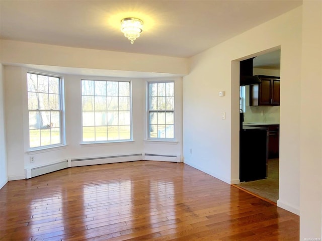 empty room with baseboard heating, a healthy amount of sunlight, and hardwood / wood-style flooring