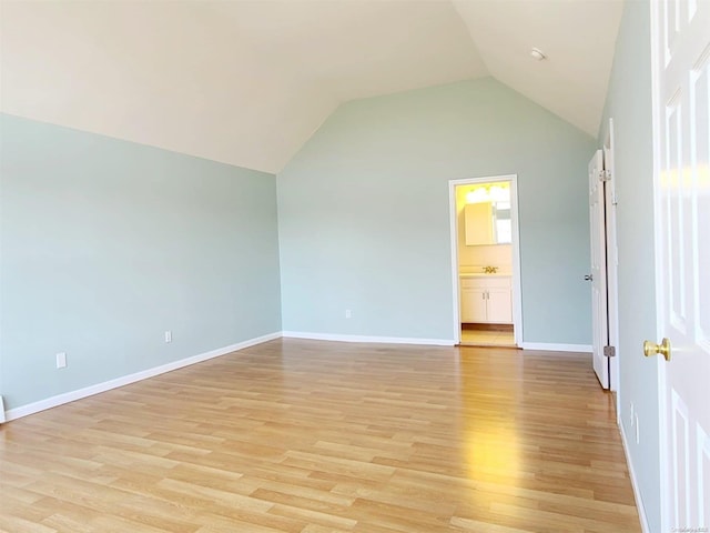 unfurnished bedroom featuring connected bathroom, light hardwood / wood-style flooring, and vaulted ceiling