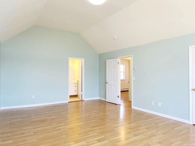 unfurnished bedroom featuring baseboard heating, ensuite bath, light hardwood / wood-style floors, and vaulted ceiling