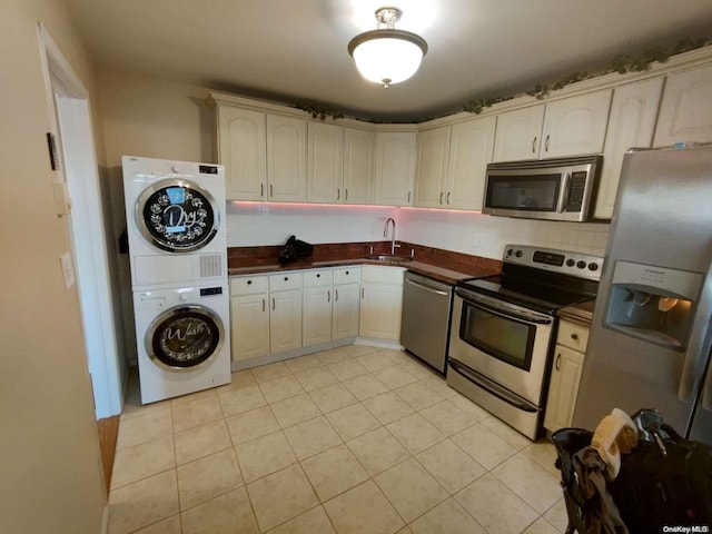 kitchen with backsplash, sink, stacked washer / drying machine, light tile patterned flooring, and stainless steel appliances