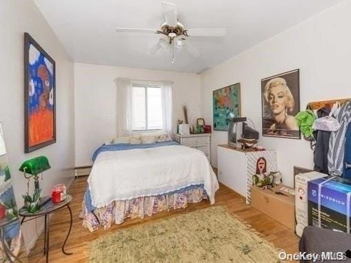 bedroom with ceiling fan, wood-type flooring, and a baseboard radiator