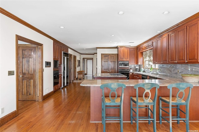 kitchen with built in appliances, kitchen peninsula, a breakfast bar area, and light hardwood / wood-style flooring