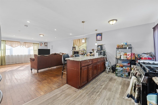 kitchen featuring pendant lighting, a center island, light stone countertops, light hardwood / wood-style floors, and a kitchen bar