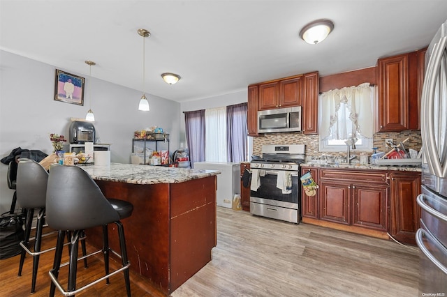 kitchen featuring light stone countertops, light hardwood / wood-style flooring, backsplash, pendant lighting, and appliances with stainless steel finishes