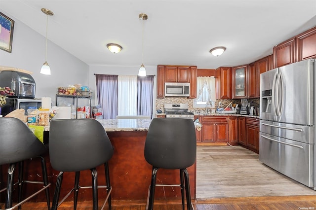 kitchen with light hardwood / wood-style flooring, decorative backsplash, decorative light fixtures, light stone counters, and stainless steel appliances