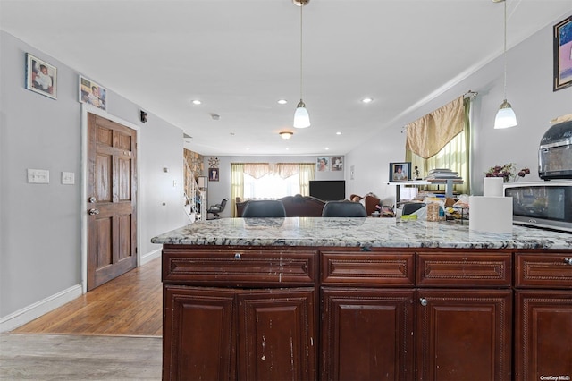 kitchen featuring light stone counters, light wood-type flooring, and hanging light fixtures