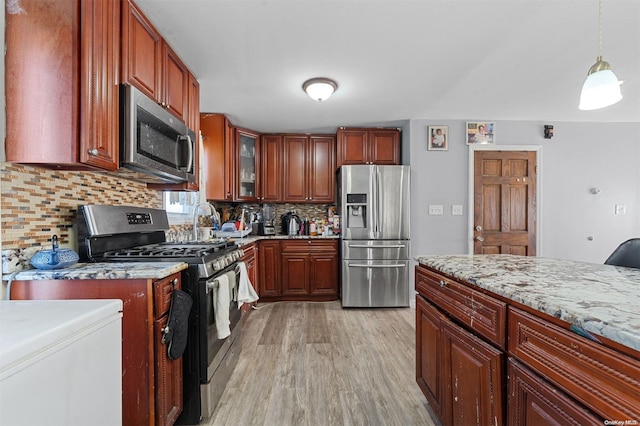 kitchen with light stone countertops, backsplash, stainless steel appliances, decorative light fixtures, and light hardwood / wood-style floors