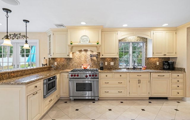 kitchen featuring dark stone counters, cream cabinets, sink, decorative light fixtures, and stainless steel appliances