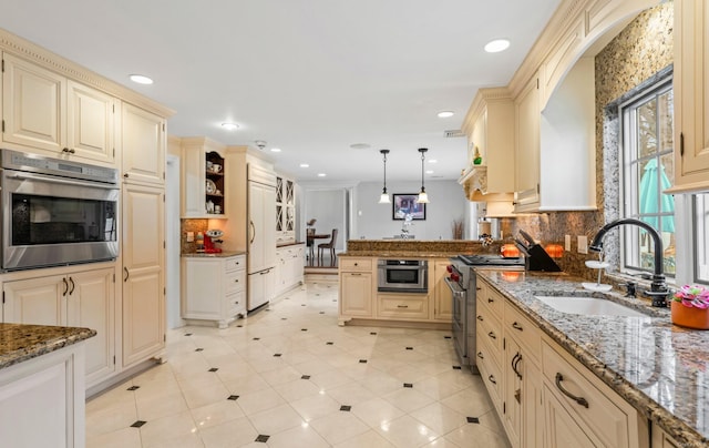 kitchen featuring tasteful backsplash, light stone counters, sink, high quality appliances, and hanging light fixtures