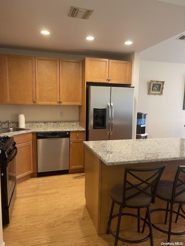 kitchen with appliances with stainless steel finishes, a kitchen breakfast bar, light stone counters, sink, and light hardwood / wood-style flooring