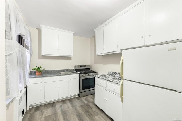 kitchen with white cabinets, white fridge, light hardwood / wood-style floors, and stainless steel range with gas stovetop