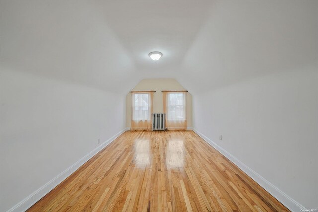 additional living space with radiator heating unit, vaulted ceiling, and light wood-type flooring