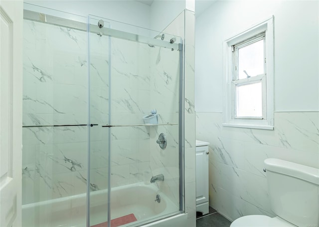 bathroom featuring combined bath / shower with glass door, toilet, and tile walls