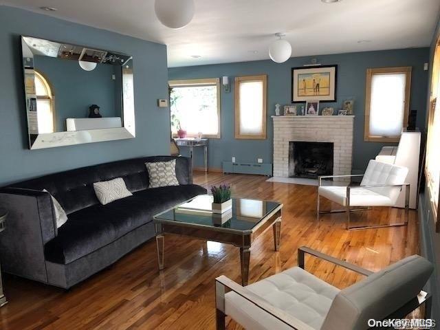 living room with baseboard heating, a fireplace, and wood-type flooring