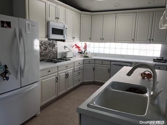 kitchen featuring white appliances, backsplash, sink, hanging light fixtures, and white cabinetry