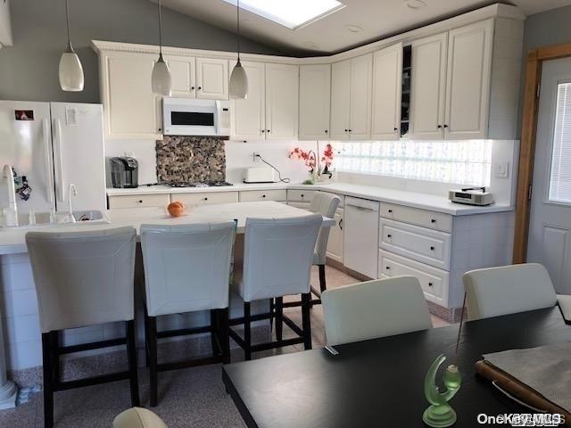 kitchen with a kitchen breakfast bar, vaulted ceiling, decorative light fixtures, white appliances, and white cabinets