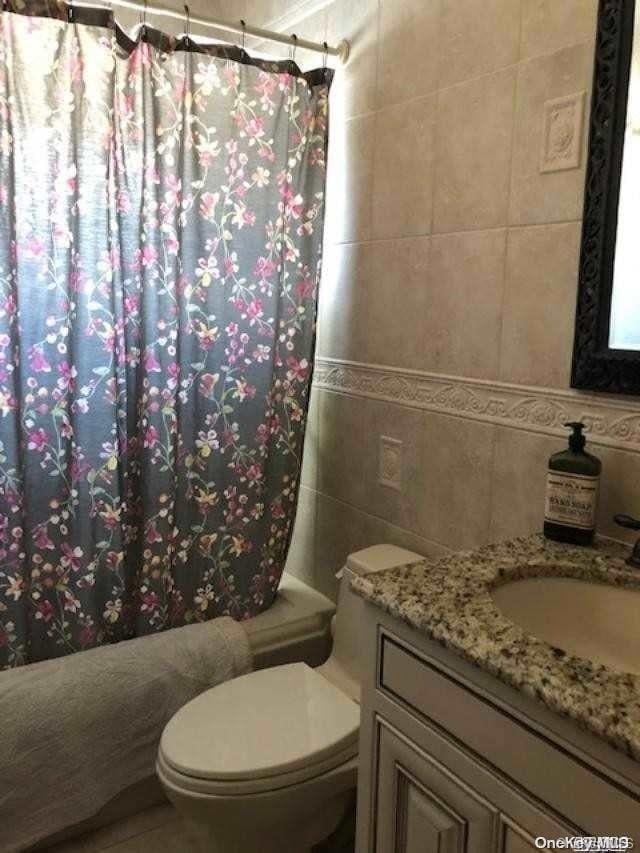 full bathroom featuring shower / bath combination with curtain, vanity, toilet, and tile walls