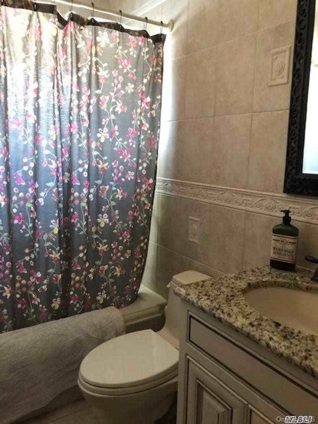 full bathroom with vanity, toilet, tile walls, and shower / tub combo with curtain