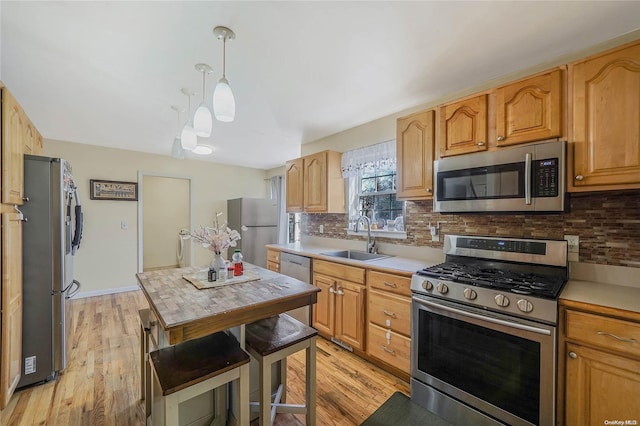 kitchen featuring sink, tasteful backsplash, pendant lighting, appliances with stainless steel finishes, and light wood-type flooring