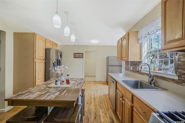 kitchen with appliances with stainless steel finishes, light wood-type flooring, tasteful backsplash, sink, and pendant lighting