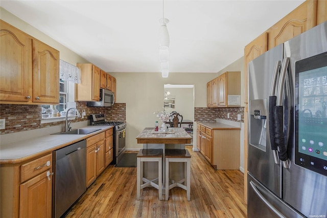 kitchen featuring stainless steel appliances, hanging light fixtures, light hardwood / wood-style floors, and sink