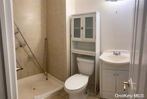 bathroom with tile patterned floors, toilet, a tile shower, and vanity