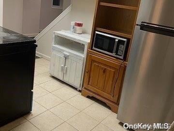 kitchen with stainless steel fridge, light tile patterned flooring, and black microwave