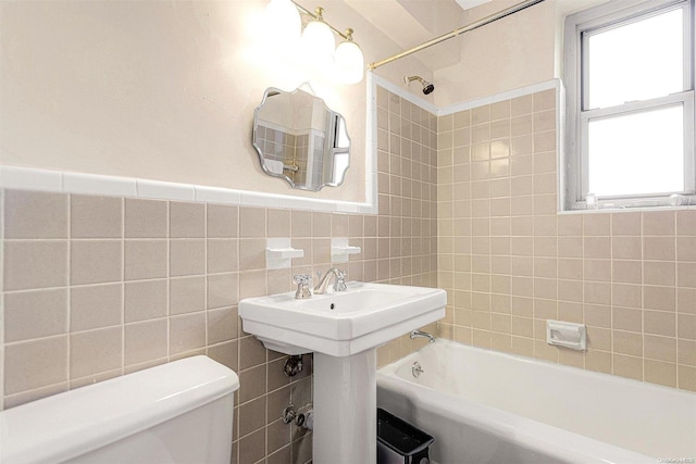 bathroom featuring tiled shower / bath combo, a healthy amount of sunlight, tile walls, and toilet