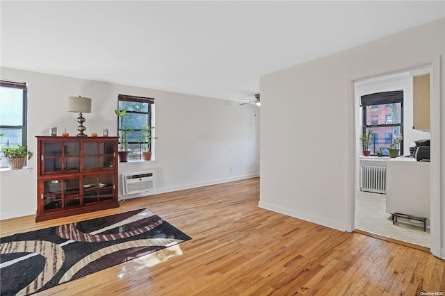 living room featuring wood-type flooring, an AC wall unit, radiator, and ceiling fan