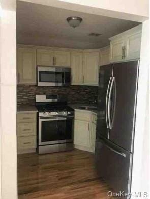 kitchen with cream cabinets, dark hardwood / wood-style flooring, stainless steel appliances, and backsplash