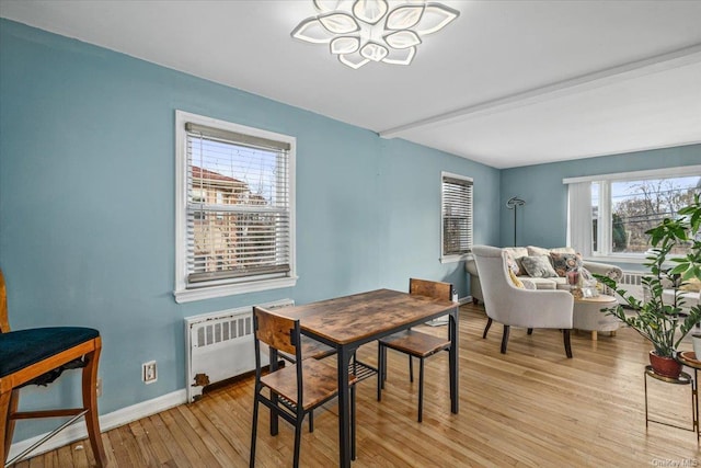 dining space with radiator, light hardwood / wood-style flooring, beamed ceiling, and a notable chandelier