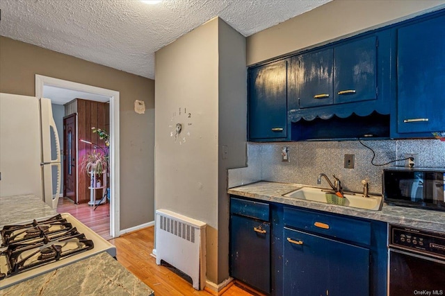 kitchen with radiator heating unit, white refrigerator, blue cabinets, and sink