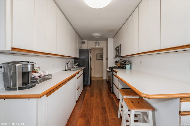 kitchen featuring dark wood-type flooring, white cabinets, a kitchen breakfast bar, sink, and appliances with stainless steel finishes